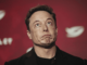 Elon Musk speaking at a press conference with a serious expression